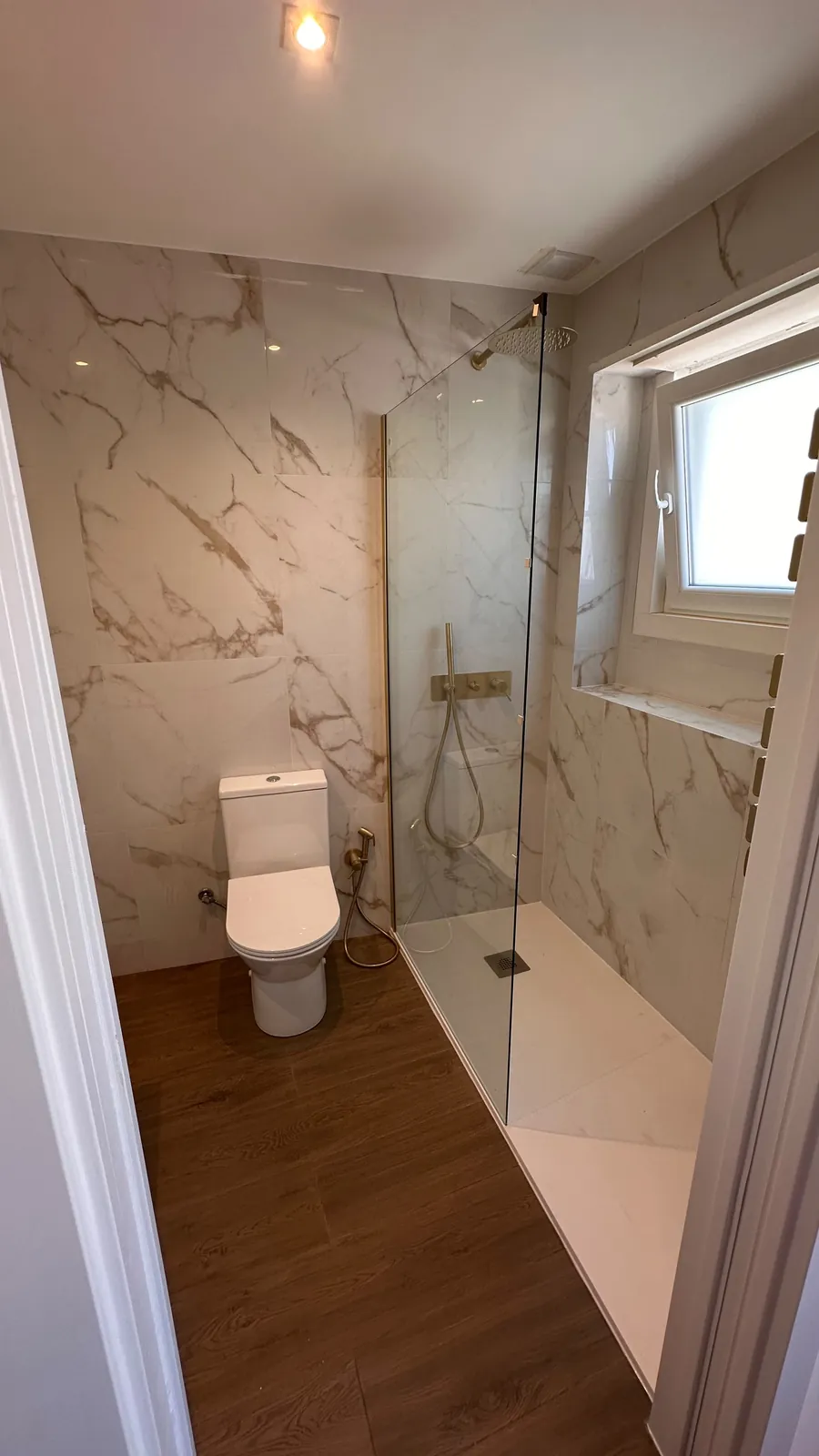 Casa de banho remodelada em Benfica, Lisboa: duche walk-in com painel de vidro e revestimento efeito mármore